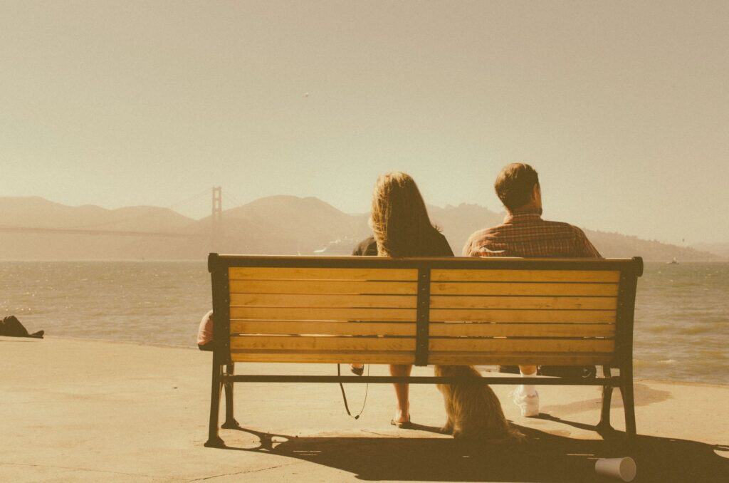 Couple sitting on a bench watching the sunset over the water.