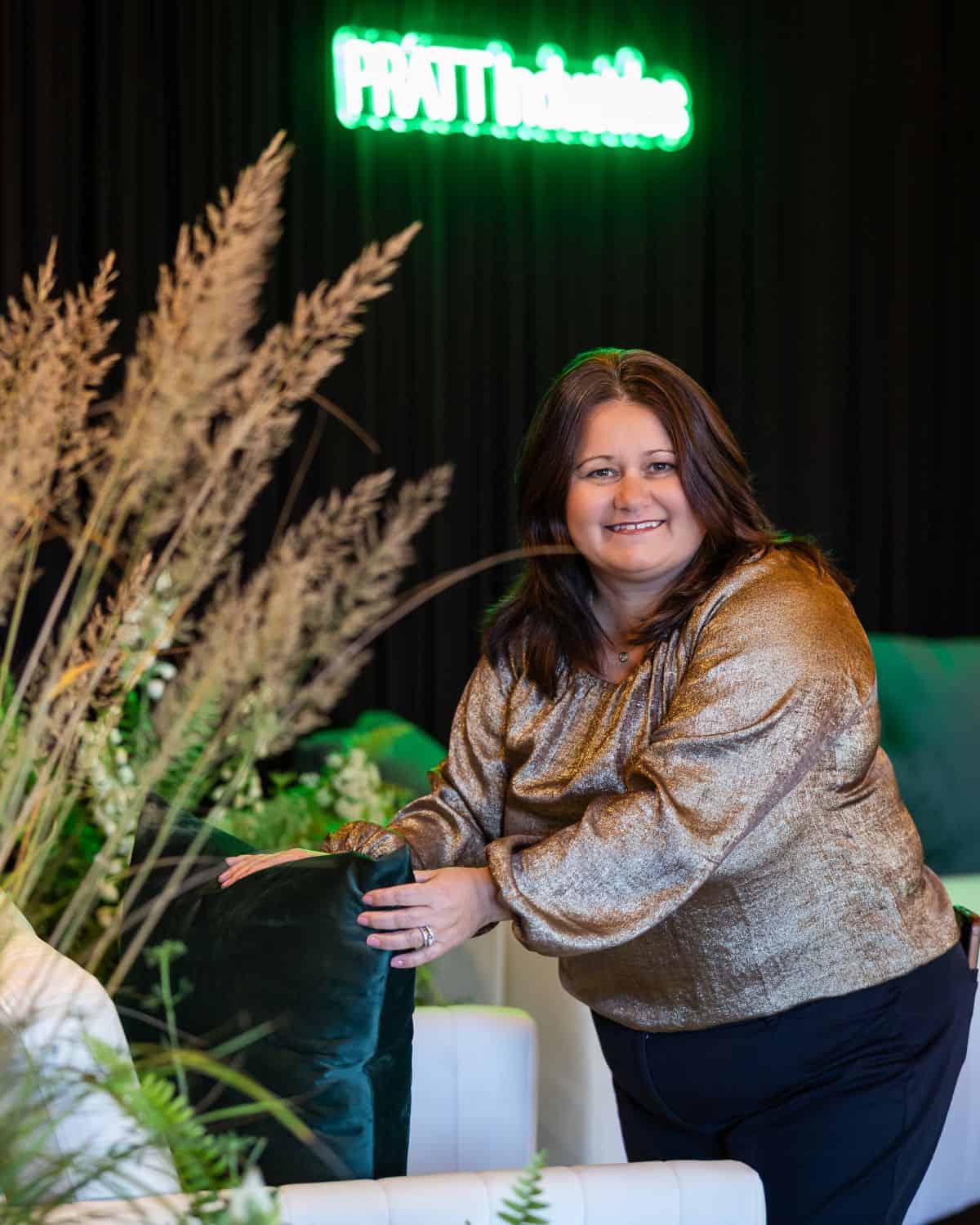 Smiling woman at SRE event planning and design showcase with plants and neon sign.