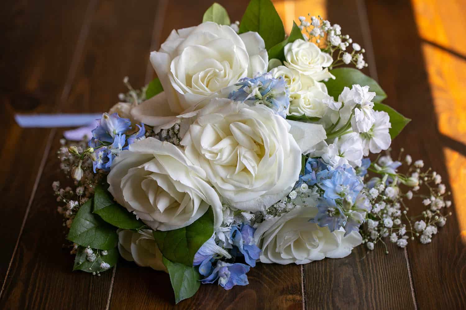 Beautiful wedding bouquet with white roses and blue accents on wooden table.