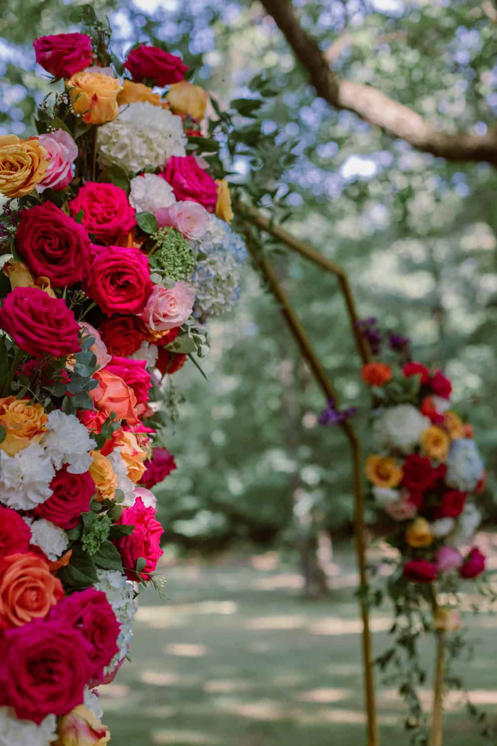 Colorful floral arch for outdoor wedding ceremony with roses and hydrangeas.